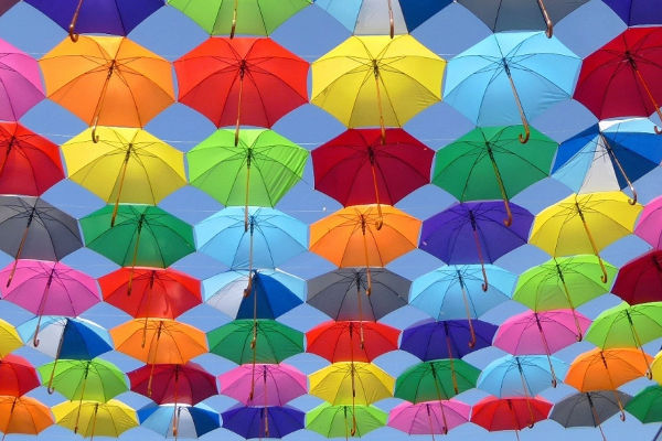 Mängder med paraplyer i olika färger upphängda på linor med den ljusblå himlen i bakgrunden.