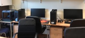 Foto på arbetsplatser med datorer, 3D skrivare och hörlurar.